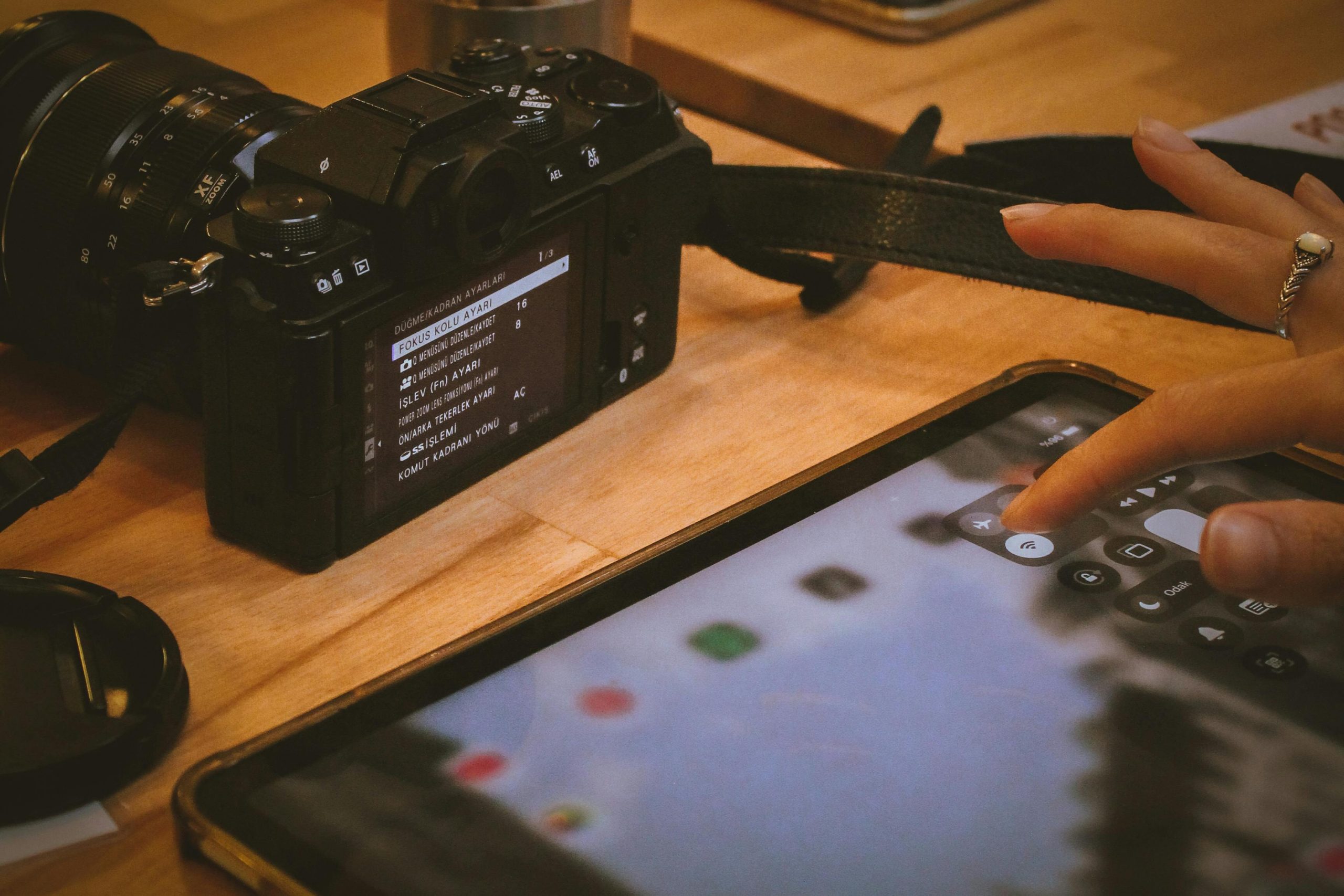 Close-up of a digital camera with lens next to a hand interacting with a tablet.